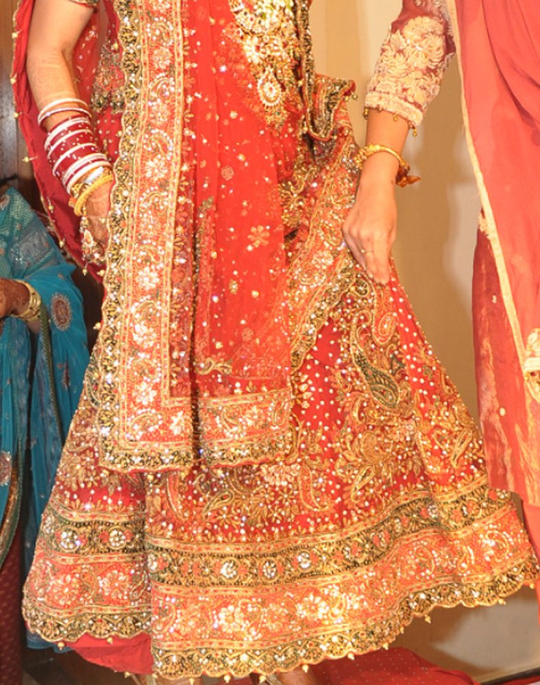 A bride's red and gold gota-embroidered lehenga and dupatta, worn with red-and-white wedding bangles.