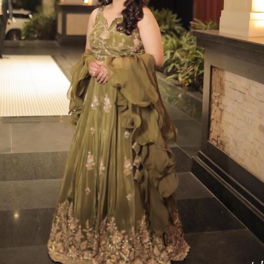Model in a moss-green ruffled gown with a draped dupatta and gold floral embroidery along the hem.