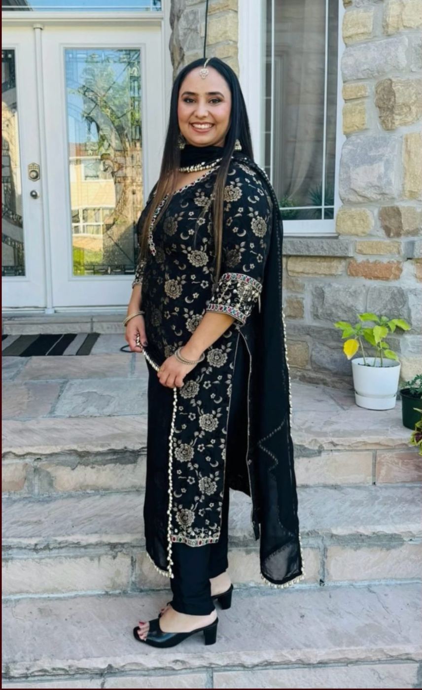 Model wearing a black Banarasi-embroidered kurta and pearl-trimmed dupatta, standing on a stone doorstep.