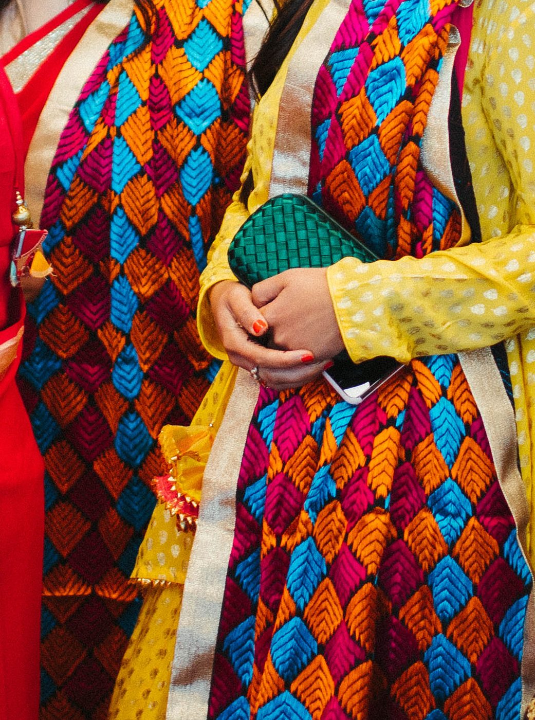 Close-up of vivid pink, orange, and turquoise Phulkari-embroidered stoles worn at a Punjabi wedding.