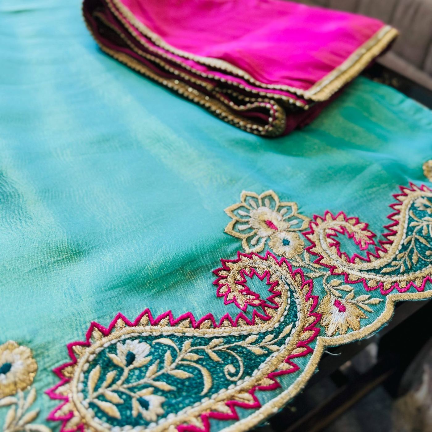 Folded turquoise dupatta with a hot-pink silk lining, edged in a gold and fuchsia paisley-embroidered border.