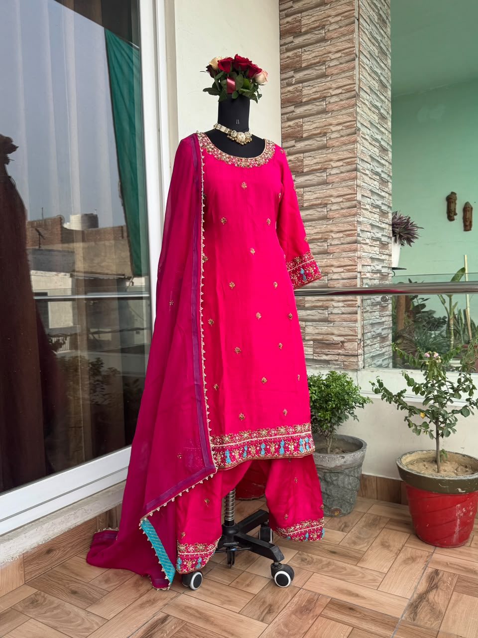 Magenta-pink suit on a mannequin with a dense gold and pearl floral embroidered hem border, plain body, and a teal-lined dupatta.