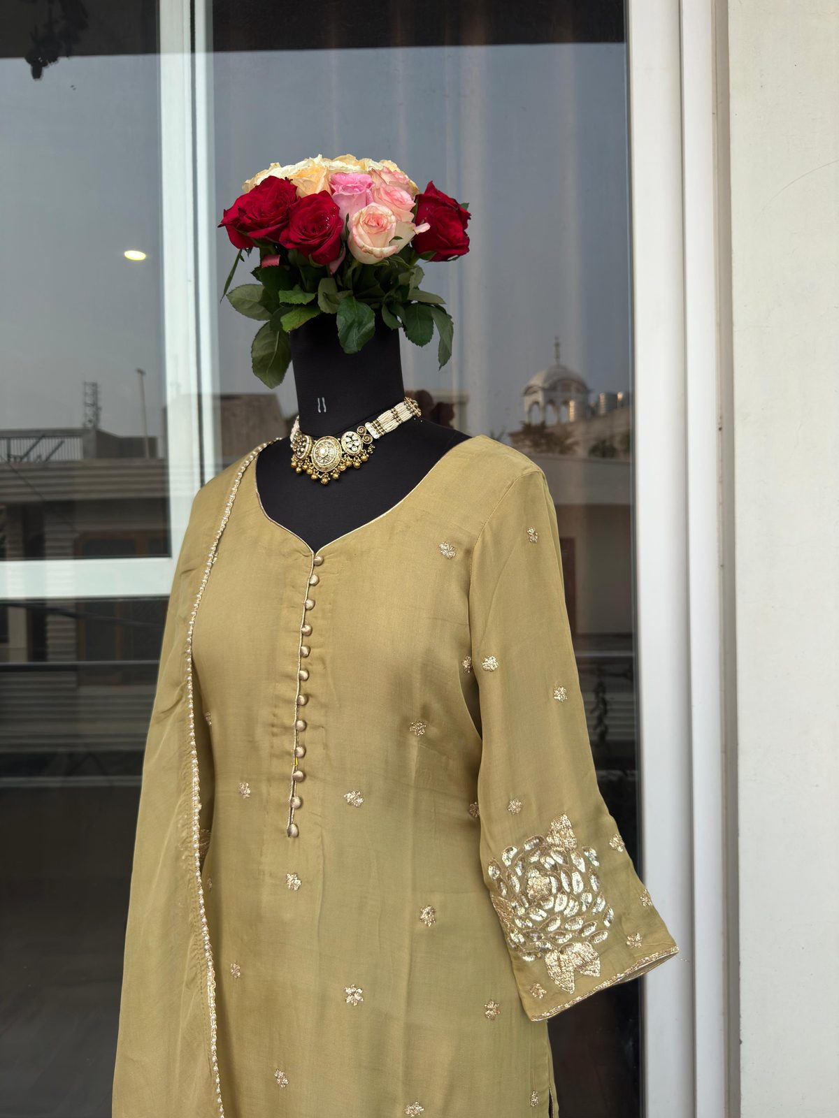 Close front view of an olive-green suit with a gold gota-embroidered floral cuff, on a mannequin, button-front placket visible.
