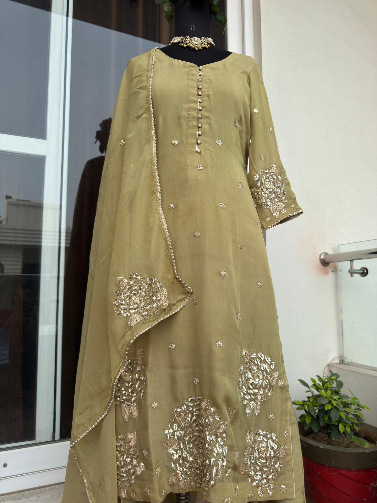 Full-length front view of the olive-green gota-embroidered suit with matching dupatta draped over the shoulder, scattered gold floral booti, and a large floral cluster embroidered at the dupatta hem.