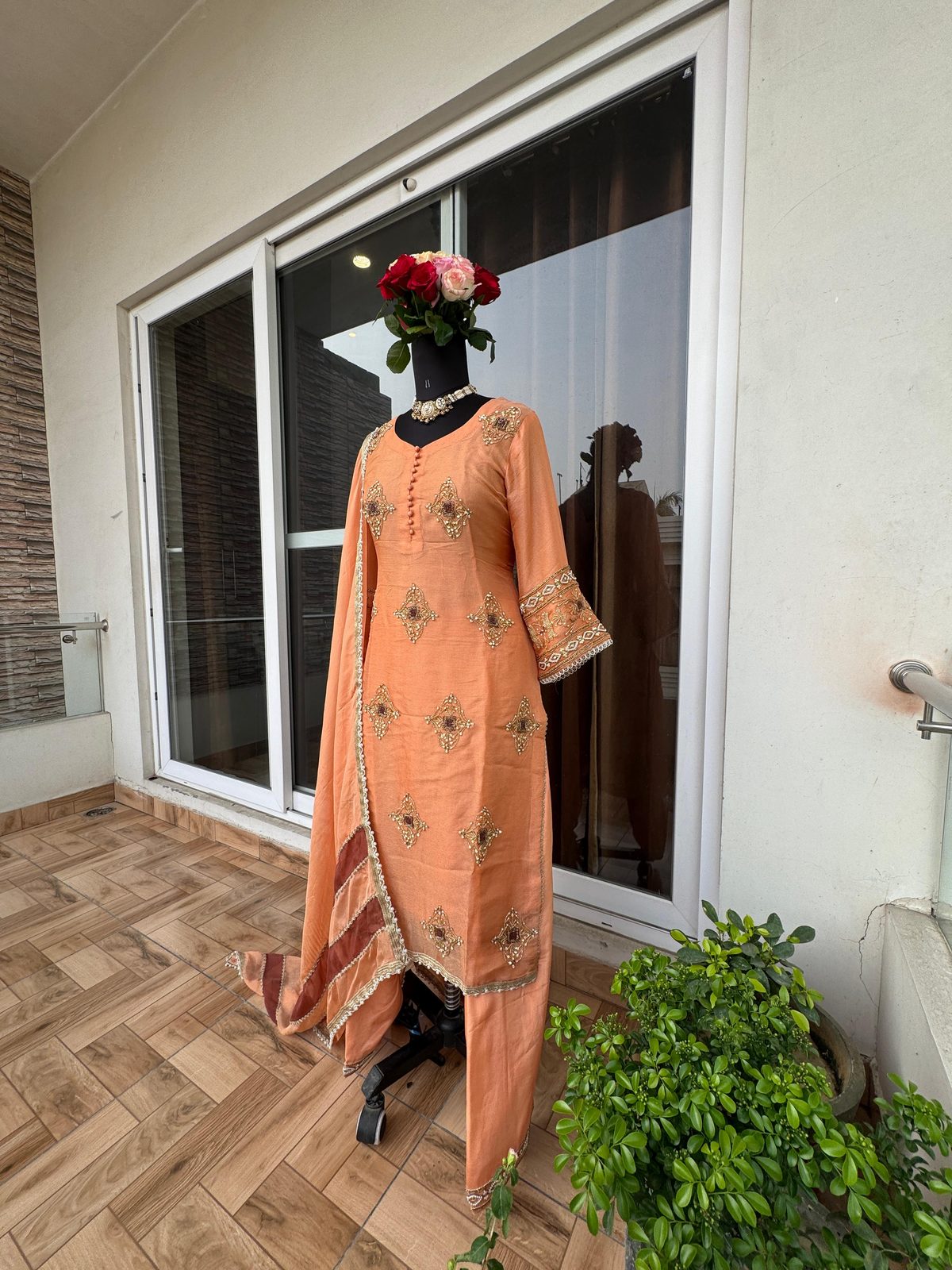 Full-length view of a peach suit on a mannequin, with gold and maroon-stone diamond-shaped embroidered motifs down the front and a striped-border dupatta.