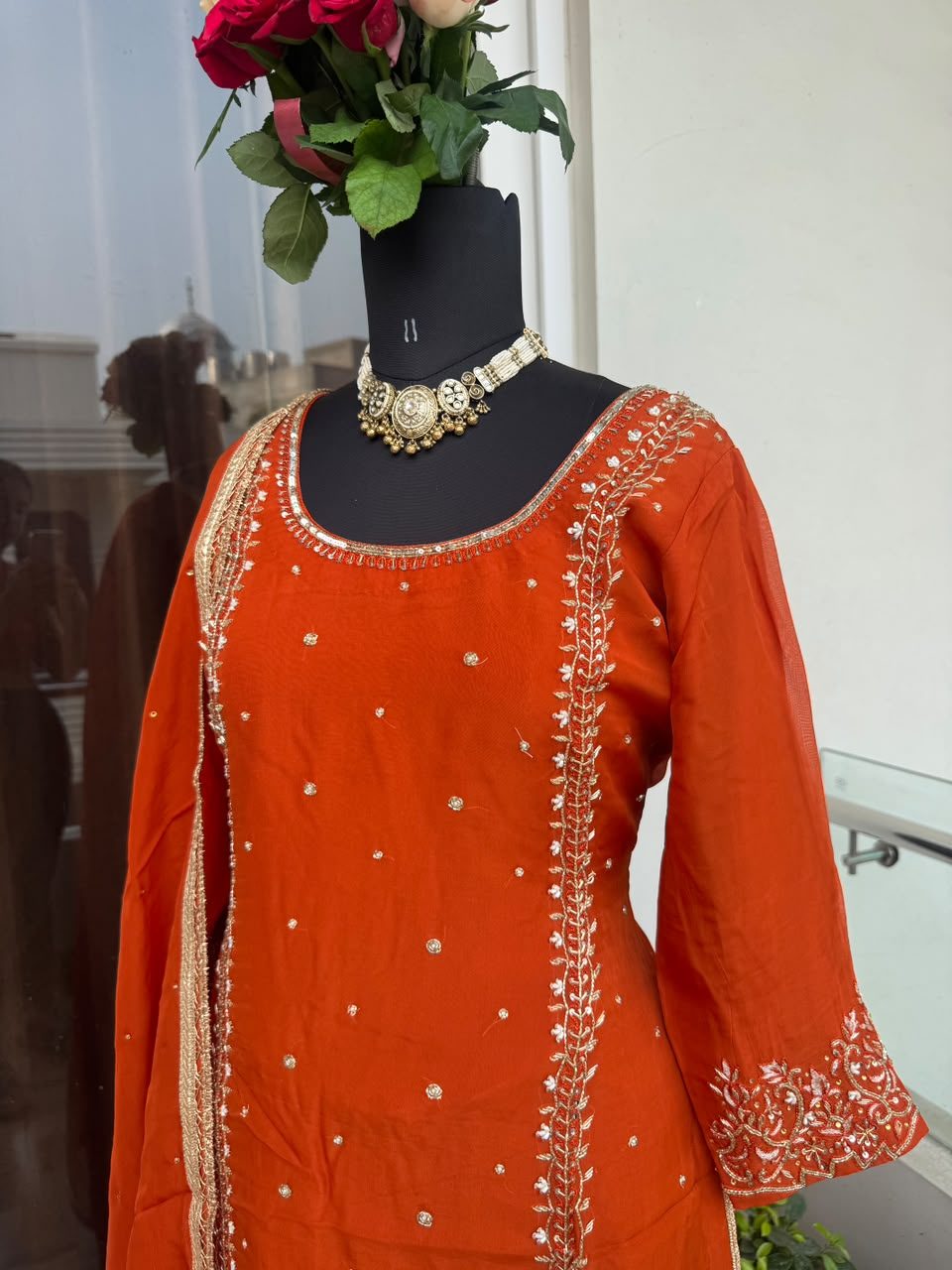 Front view of a rust-orange kurta with white gota vine embroidery down the front placket and scattered sequin dots, on a mannequin.